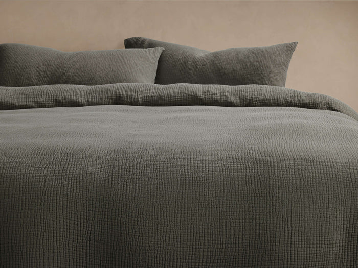 Deep sage green Cotton Gauze Duvet Set, featuring a crinkled duvet cover and two matching shams on a bed against a light wall.