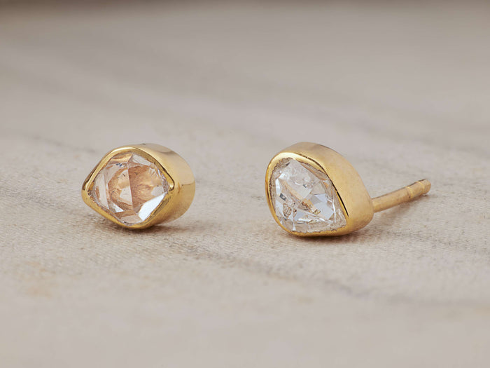 Darian Herk Diamond Bezel Stud Earrings featuring raw Herkimer Diamonds in gold-plated settings on a textured surface.