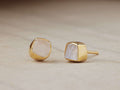 Darian Moonstone Bezel Stud Earrings with luminous moonstone in gold-plated settings, textured stone with unique shape on wooden surface.