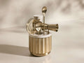 Front view of the golden Dayan Bar Tools set, including a fluted brass holder with a white marble top, strainer, jigger, and spoons.