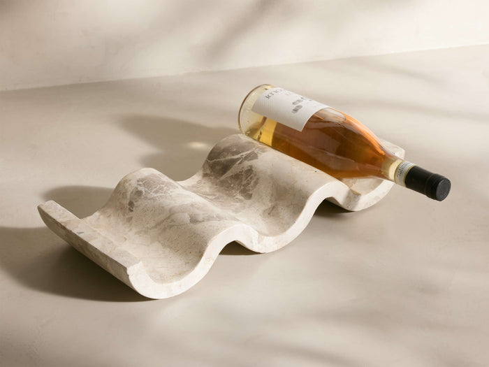 Angled view of the wavy, creamy white Dayana Wine Rack, crafted from natural marble with gray veining, holding a wine bottle.