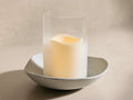 Front view of Delos Wave Hurricane™ featuring a grey cast aluminum wavy base and frosted-glass cloche with a warm white glowing candle.