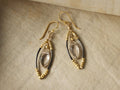 Delphine Earrings with gold vermeil French wire, smoky quartz center, and oxidized silver accents on a beige surface.