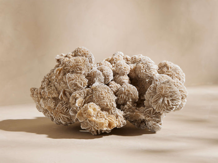 Large sandy Desert Rose mineral cluster with intricate, rose-like formations on a light beige surface.