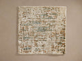 Devi Rug Swatch. Rectangular swatch with textured cream base, abstract brown and muted green lines, against a beige wall.