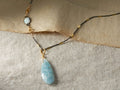 Devyn Necklace on fabric backdrop, features oxidized silver chain with gold accents, opal, and large aquamarine teardrop pendant.