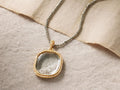 Diamond Shaker Cush Necklace features a gold-plated pendant with loose diamonds on a pyrite bead chain, lying on fabric.