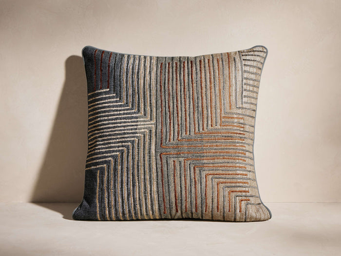 Front view of a square pillow featuring a woven geometric maze pattern in navy, light beige, and terracotta colors.