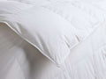 Close-up of the white quilted comforter, folded over to show its plush texture and neatly stitched edges.