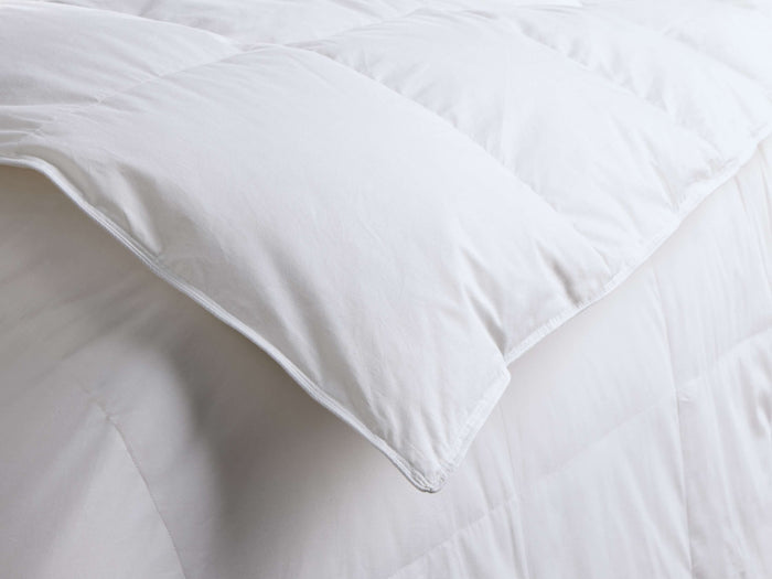 Close-up of the white quilted comforter, folded over to show its plush texture and neatly stitched edges.