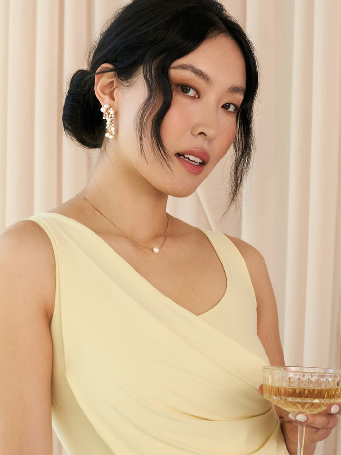 Woman in a light yellow dress holding a glass of champagne against a neutral background