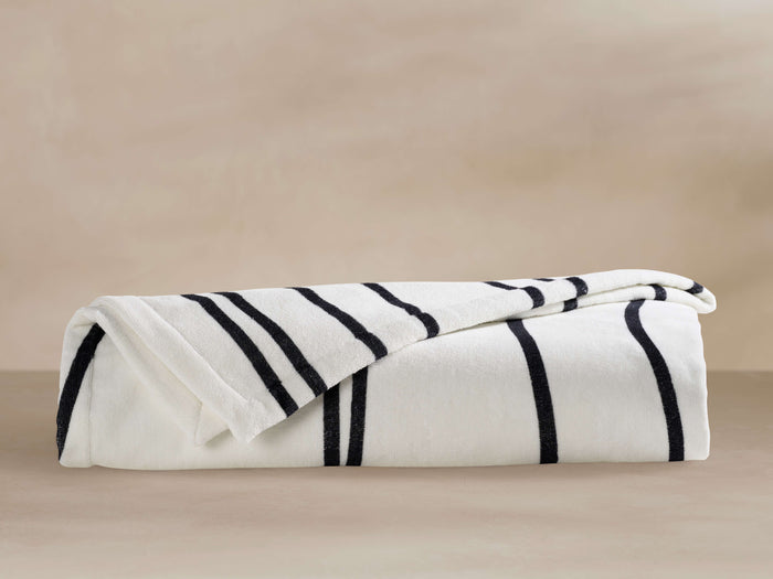 Folded Dunes Beach Towel, white with thick black vertical stripes in "Meteorite" color, lying on a light neutral surface.