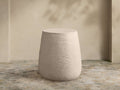 Eden Outdoor End Table. Light tan, round concrete table with distinct horizontal ribbed sides, on a stone patio.