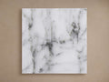 Square Edgewater Outdoor Finish Board in white faux marble, featuring dark grey veining, against a tan wall.