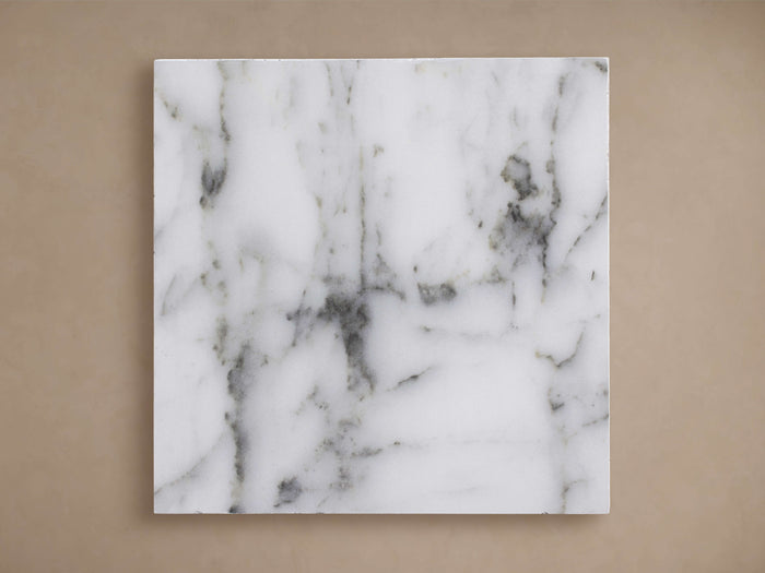 Square Edgewater Outdoor Finish Board in white faux marble, featuring dark grey veining, against a tan wall.