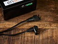 Enouvation E6 Motion Battery Pack Splitter Cable on wood surface, showing two black connectors and a battery pack with green LED indicators.