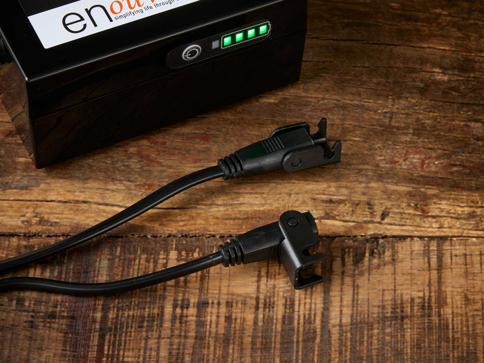 Enouvation E6 Motion Battery Pack Splitter Cable on wood surface, showing two black connectors and a battery pack with green LED indicators.