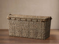 Natural rectangular handwoven seagrass Entry Console Basket with a matching lid and rope trim, on a wood floor.