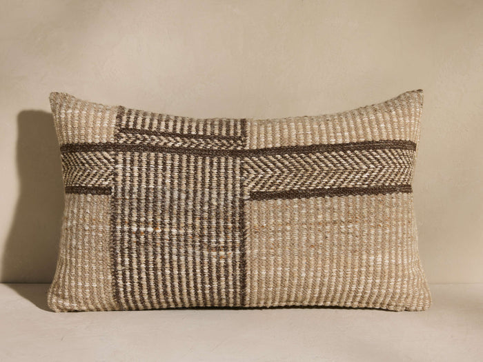 Esencia Herringbone Pillow: rectangular, woven beige & dark brown with geometric herringbone stripes, against a light wall.