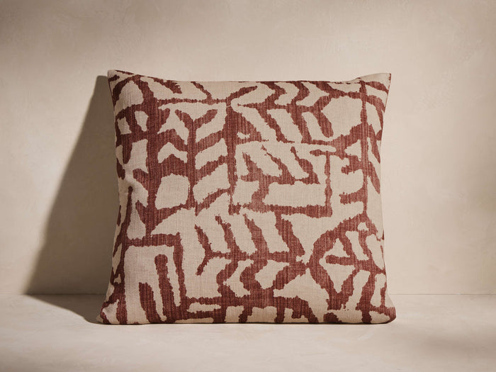 Estella Pillow, square, beige cotton-linen with bold red-brown abstract pattern, upright against a light wall.