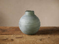 Hand-etched Etrusca Vase, muted green glass with rippled texture, on a rustic wooden table against a soft background.