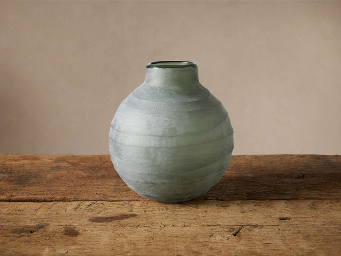 Hand-etched Etrusca Vase, muted green glass with rippled texture, on a rustic wooden table against a soft background.