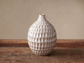 Eva Bud Vase, light beige ceramic with a sculpted honeycomb texture, standing on a rustic wooden surface.