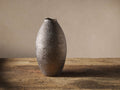 Tall, oval Eva vase with a dark, glossy, dimpled metallic finish, standing upright on a rustic wooden surface.