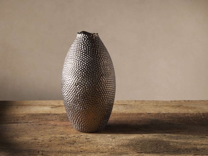 Tall, oval Eva vase with a dark, glossy, dimpled metallic finish, standing upright on a rustic wooden surface.