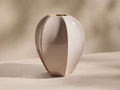 Glossy light beige ceramic Eva Seedpod Vase with a faceted, bulging shape and subtle brown edges, standing upright on a soft beige surface.