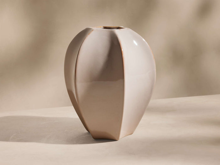 Glossy light beige ceramic Eva Seedpod Vase with a faceted, bulging shape and subtle brown edges, standing upright on a soft beige surface.