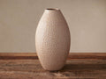 Tall, oval Eva Vase, light beige & gold ceramic with textured honeycomb pattern, stands upright on a rustic wooden surface.