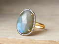 Evelina Labradorite Ring with an oval labradorite stone, surrounded by diamonds, set on a gold and black rhodium plated band.
