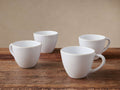 Four white Evora stoneware mugs with unglazed rims, handcrafted, arranged on a rustic wooden table.