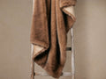 Fairbanks Faux Fur Throw in sable, draped on a rustic wooden ladder, showcasing plush brown fur and light tan microfiber back.