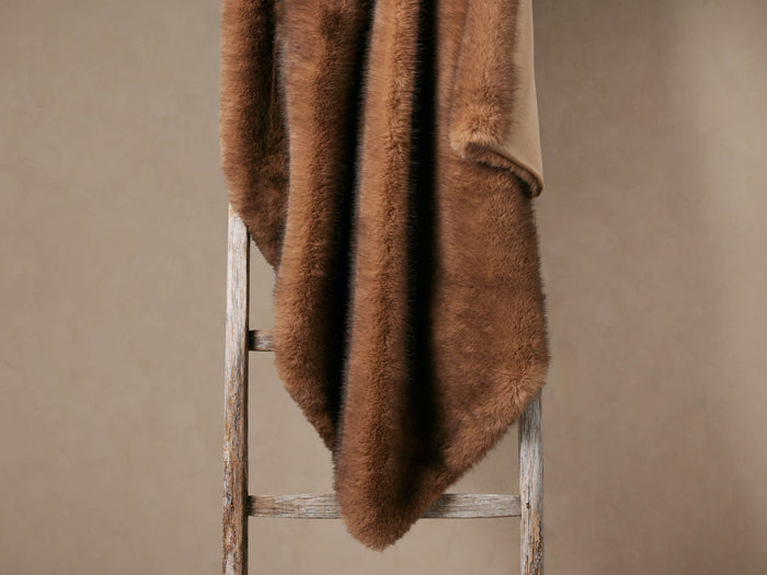 Fairbanks Oversized Faux Fur Throw, plush brown, draped over a rustic wooden ladder, with tan microfiber back visible.