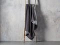 Faux Fur Sherpa Throw in dark gray, draped over a wooden ladder against a textured gray wall, showcasing its soft texture and casual elegance.