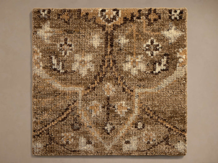 Overhead view of a square rug with a dense, looped texture, featuring an intricate traditional pattern in shades of brown, beige, and cream.