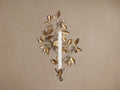 Champagne gold floral wall taper holder with sculptural leaves and bead details, holding a white candle, on a beige wall.