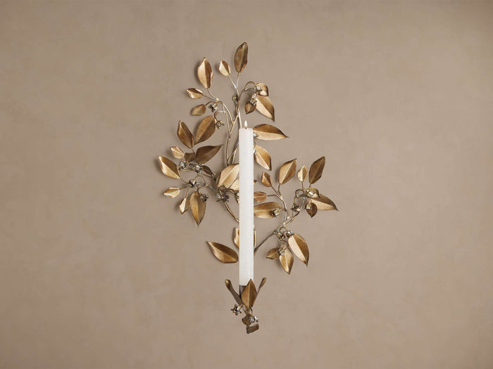 Champagne gold floral wall taper holder with sculptural leaves and bead details, holding a white candle, on a beige wall.