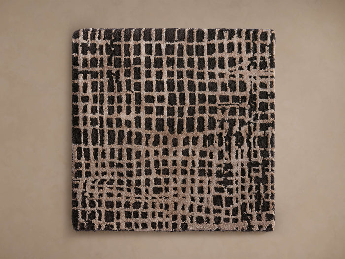 A square rug with an abstract grid pattern in black and light brown colors, displayed on a neutral background.