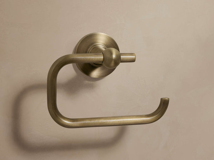 Fulton Toilet Paper Holder in antique brass, mounted on wall. Features an open end with a slight curve and round base.