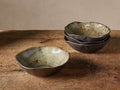 Gallatin Pasta Bowls. One front, three stacked behind, on wood. Dark, wavy edges, green/brown reactive glazed interior.