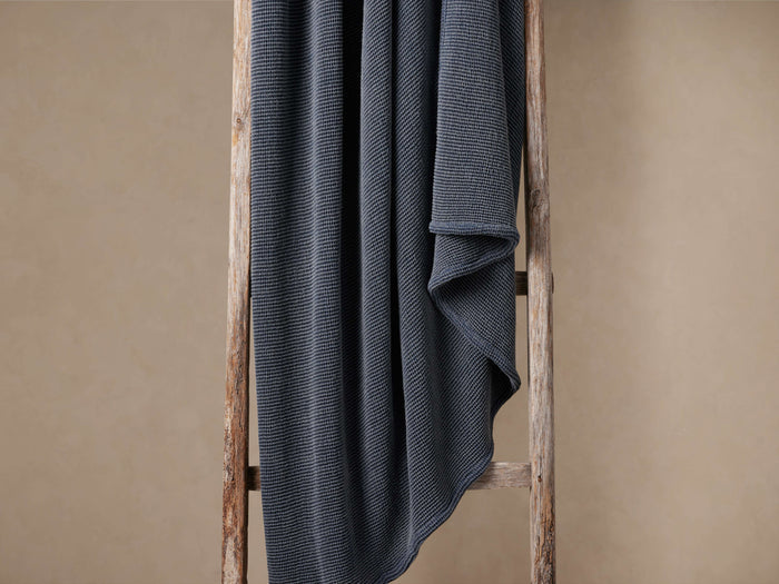 Indigo garment-dyed throw with a luxurious waffle pattern, softly draped over a rustic wooden ladder.