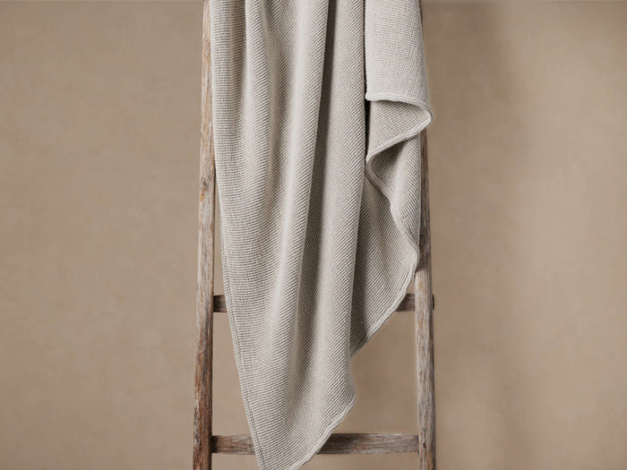 Mist-colored garment-dyed throw with waffle pattern, casually draped over a rustic wooden ladder against a neutral wall.