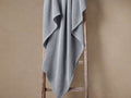 Sky blue garment-dyed throw blanket with waffle texture draped casually over a rustic wooden ladder against a light brown wall.