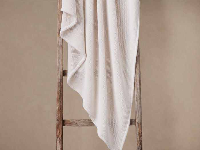 White Garment-Dyed Throw with luxurious waffle pattern draped softly over a rustic wooden ladder.