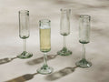 Four handblown Granada Champagne Glasses made from recycled glass. One is filled with champagne, three are empty.