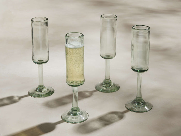 Four handblown Granada Champagne Glasses made from recycled glass. One is filled with champagne, three are empty.