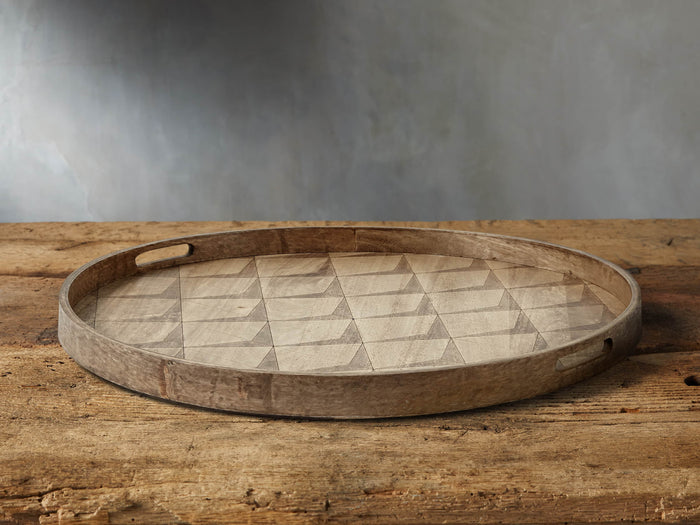 Granada Round Tray made of mango wood on a rustic wooden surface, featuring an alternating light and dark geometric pattern.